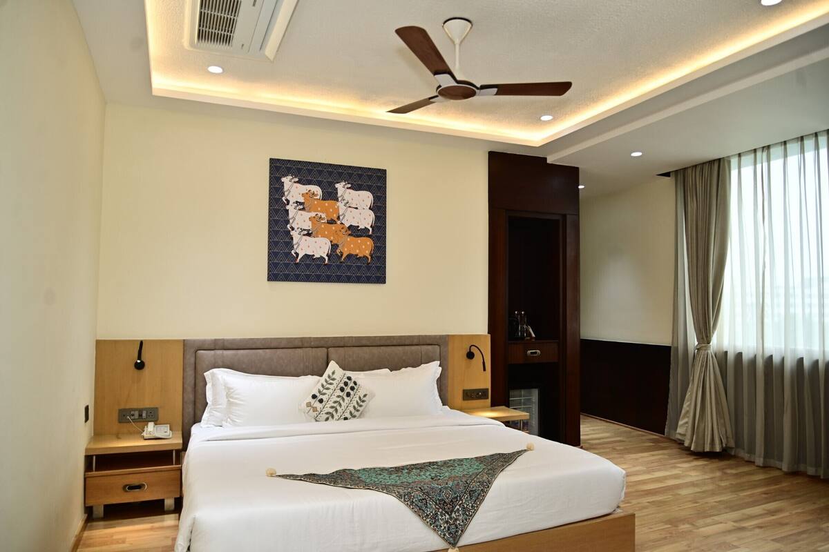 A neatly made bed with white linens and a decorative throw, a ceiling fan, and a wall-mounted artwork depicting animals.