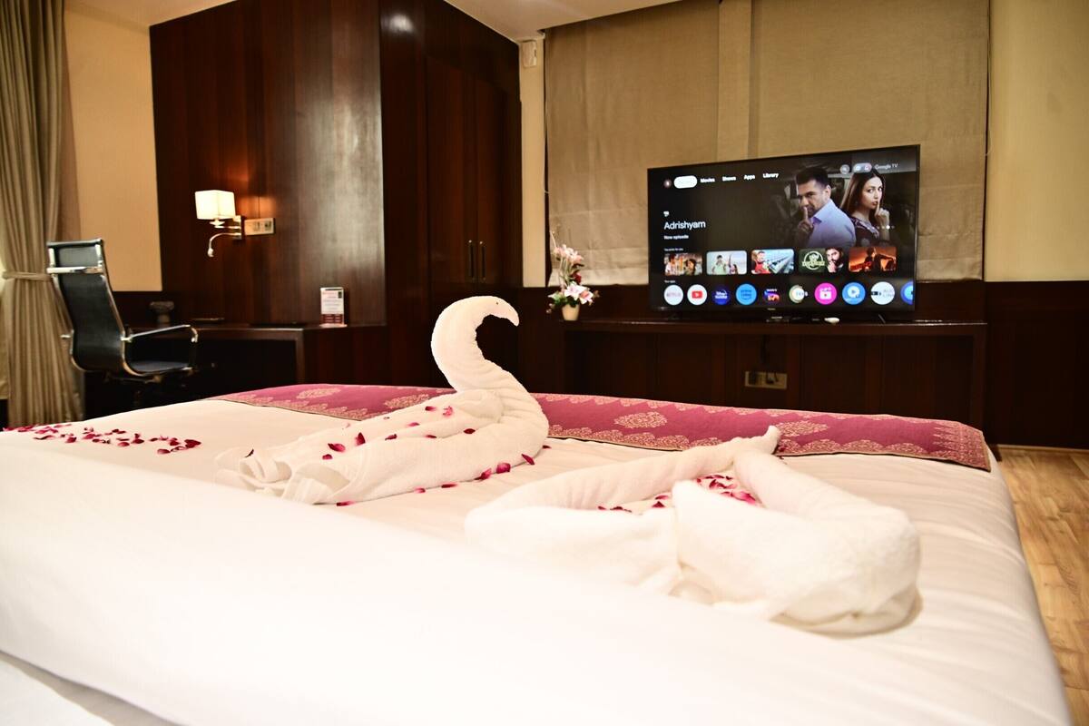 A hotel room with a large bed, a TV on the wall, a desk, and a chair.