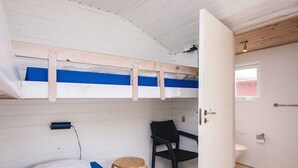Un lit superposé avec un bureau et une chaise, des toilettes et un petit tabouret.