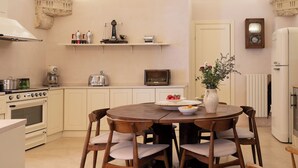A kitchen with a large arched window, wooden chairs, a round table, and various kitchen appliances. - Casa a Corte (Nardò)