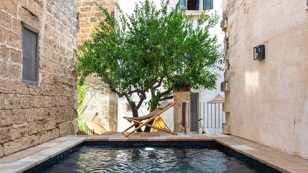 A pool area with a wooden lounge chair, a tree, and stone walls. - Casa a Corte (Nardò)