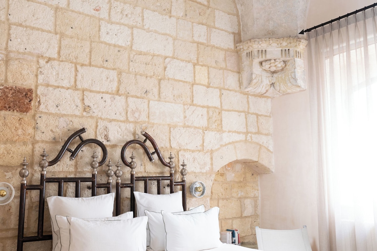 A bedroom with a brick wall, a bed with white bedding, a wooden headboard, and a window with curtains.