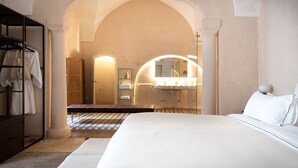 A hotel room with a large bed, a wardrobe, a bench, a bathroom with a vanity and mirror, and an arched doorway. - Casa a Corte (Nardò)