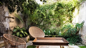 A rustic outdoor seating area with wicker chairs and a wooden table, surrounded by lush greenery and a stone wall. - Casa a Corte (Nardò)