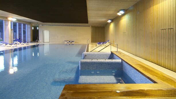 Una piscina al coperto con acqua cristallina, gradini d'accesso e lettini lungo il bordo.