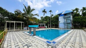 Una piscina con plataforma de azulejos, una torre de salvavidas y palmeras al fondo.