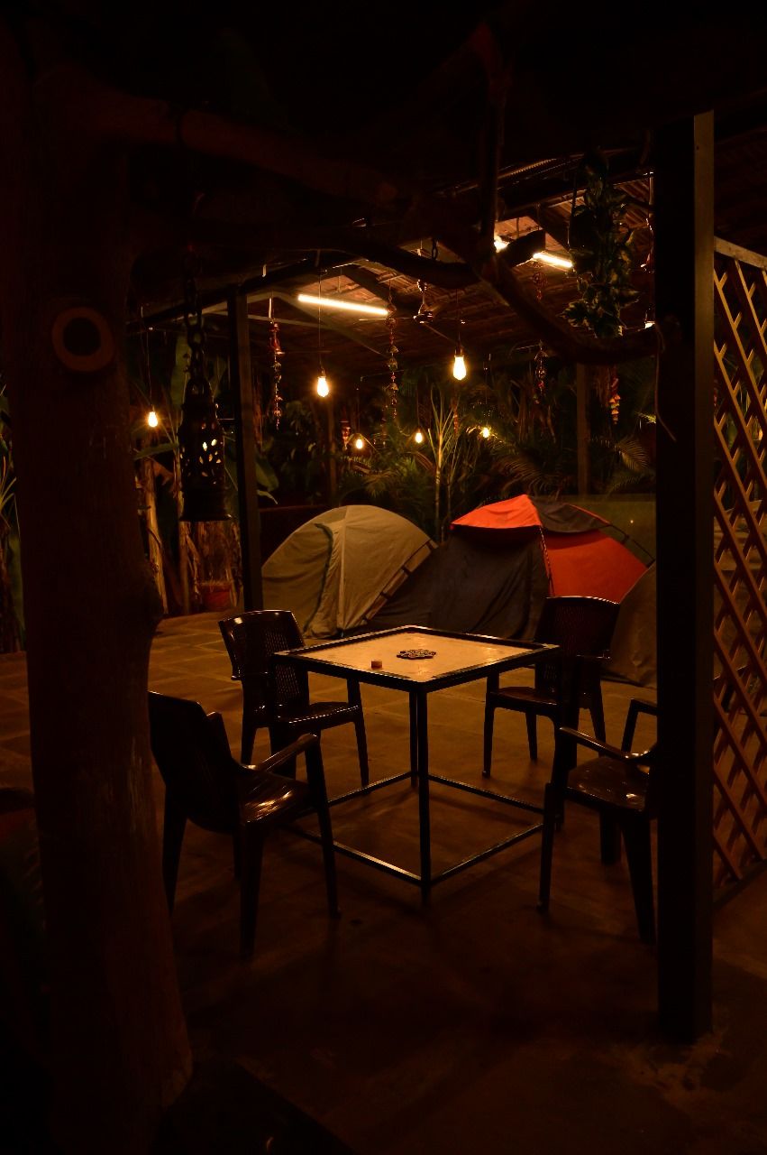 A covered outdoor seating area with tables and chairs, surrounded by trees and plants.