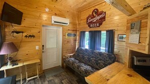 A cozy cabin interior with a wooden ceiling, a couch, a table, and a sign for Leinenkugel's beer.