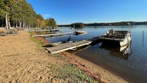 A lakeside dock with boats, a sandy beach, and a row of trees.