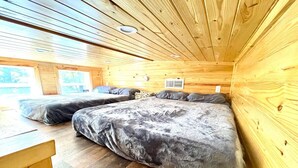 A cozy cabin interior with wooden walls and floors, two beds with grey bedding, and a small table.