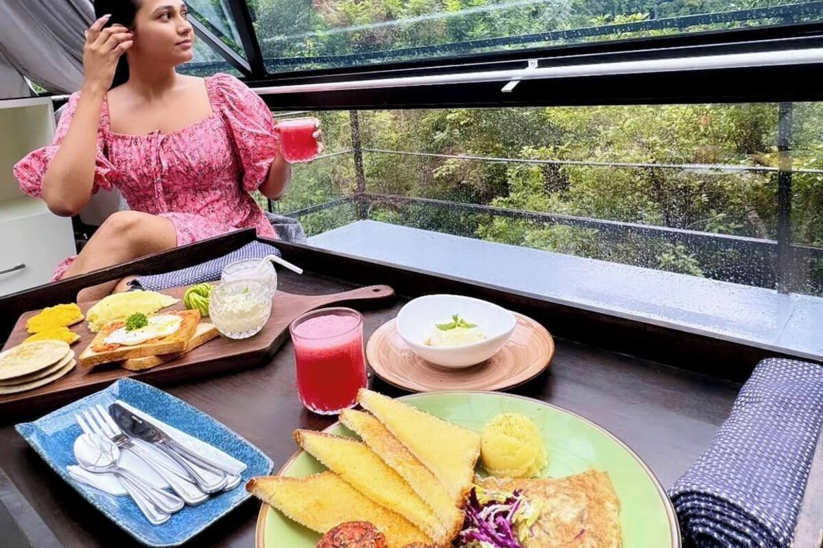 A dining table with food and a person in a pink top, overlooking a mountainous landscape.