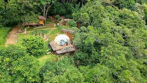 An aerial view of a secluded eco-lodge surrounded by dense forest, featuring a dome-shaped structure, wooden cabins, and a clear path. - Glamping by Offtrek (Medamahanuwara)