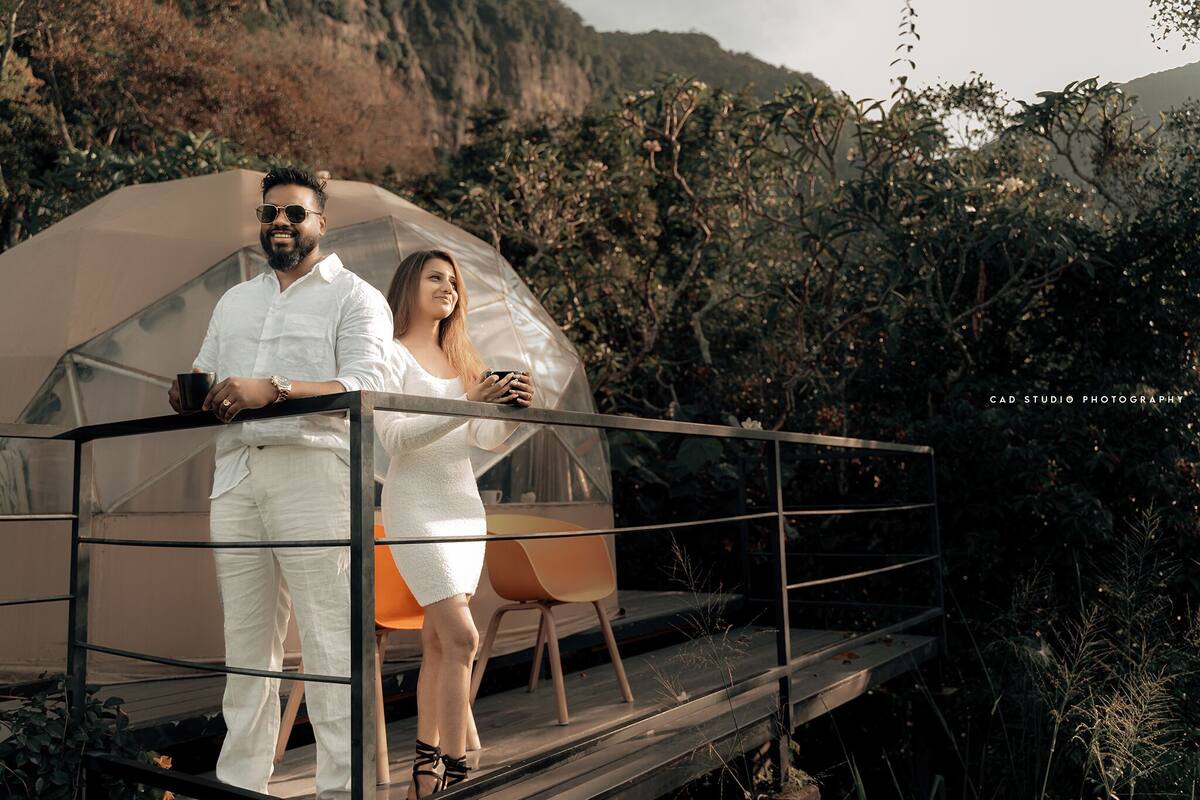 A couple standing on a glass bridge with a mountain backdrop.