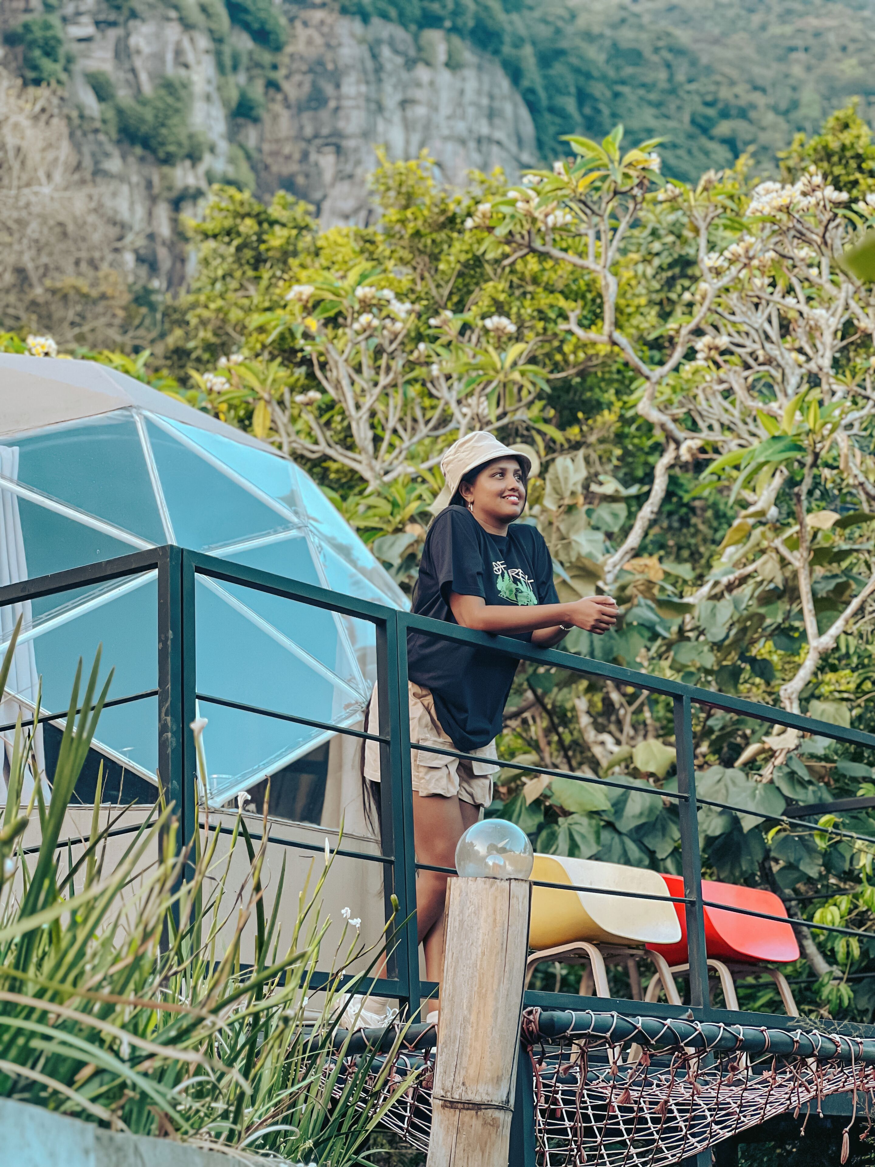 A person standing near a blue geodesic dome structure, with a chair and a rope hammock nearby.