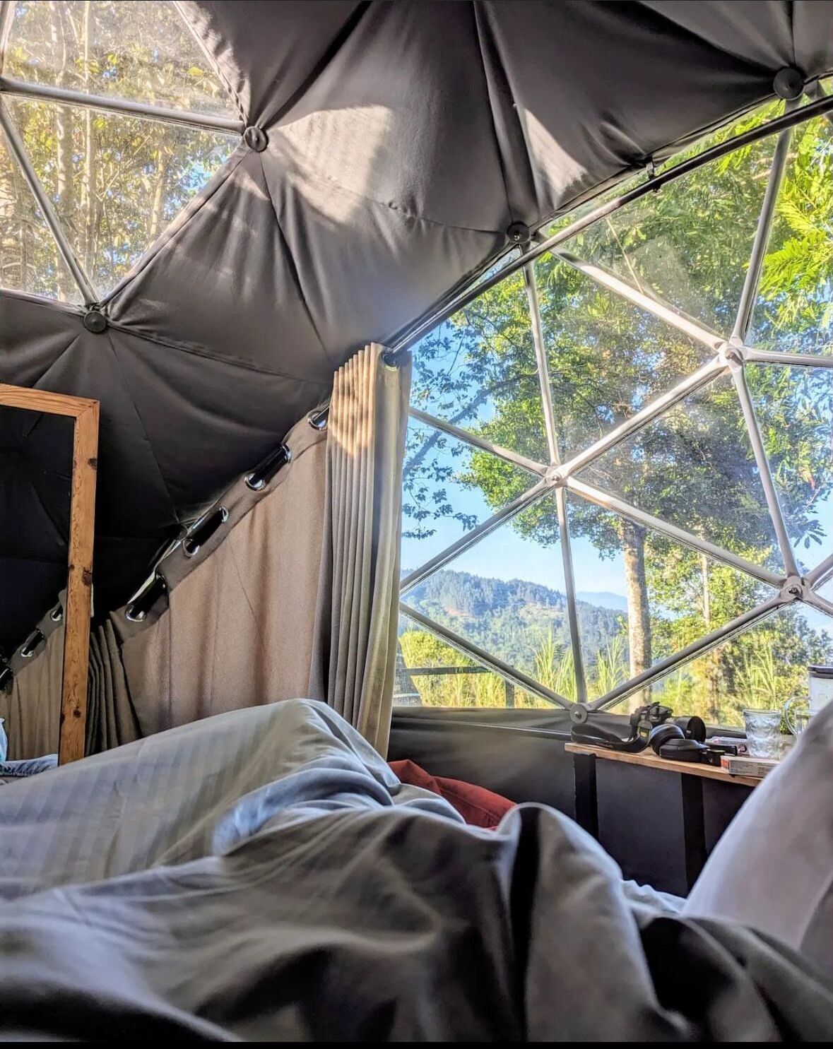 Una tienda de campaña con un diseño geométrico, una cama y vistas a árboles y colinas.
