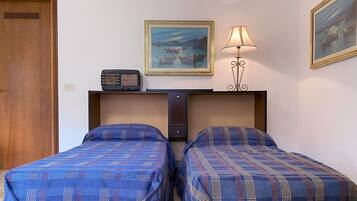 A room with two beds, a radio, a lamp, and two paintings on the wall.