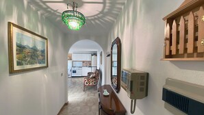 A hallway with a chandelier, a framed painting, a wooden cabinet, a mirror, and a wall-mounted thermostat. - PERSEVERANTIA (Subiaco)