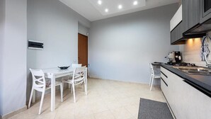 Een moderne keuken met een eethoek, met een witte tafel en stoelen, een inbouwfornuis en een zwart aanrecht.