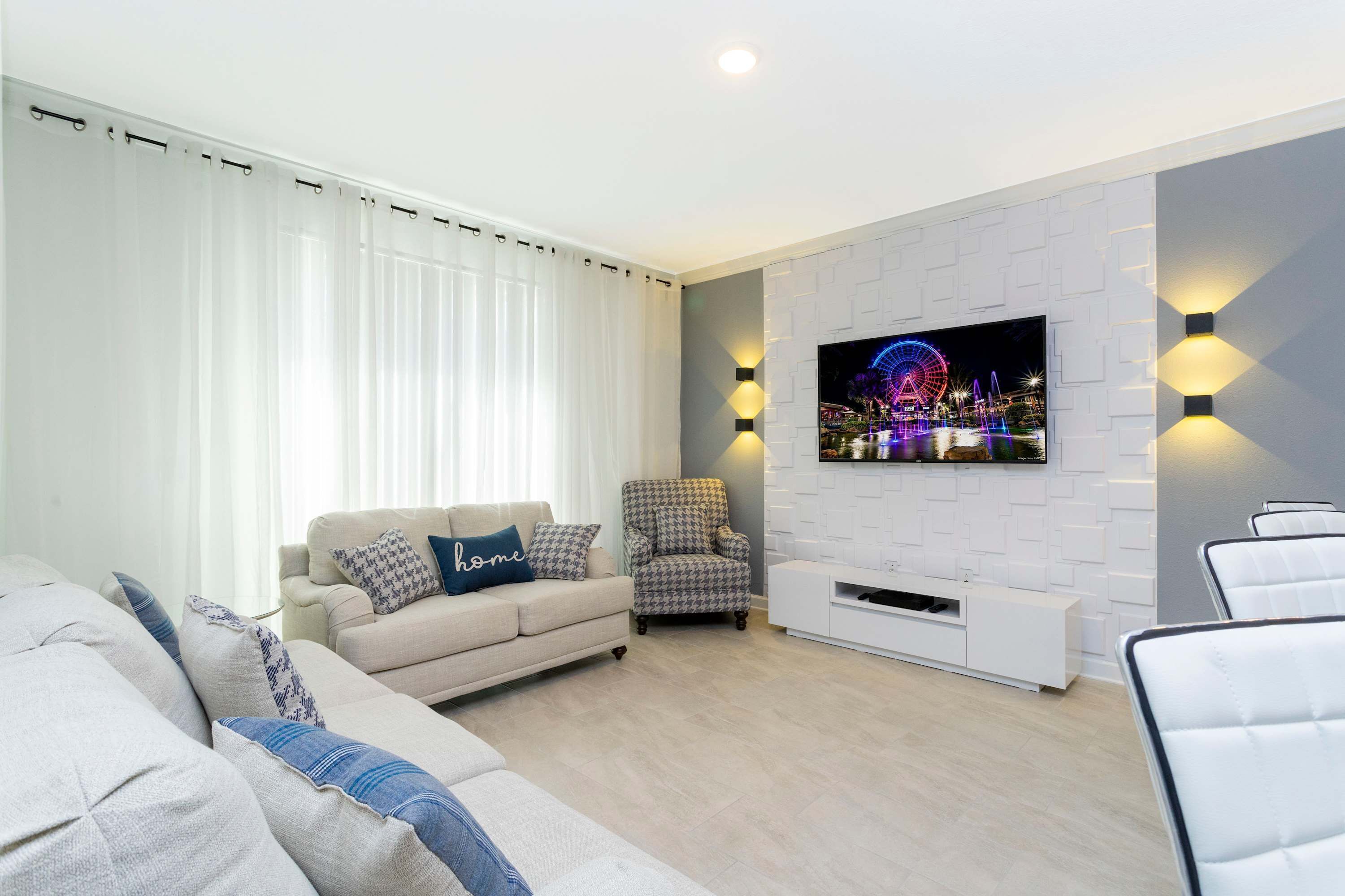 A modern living room with a sofa, armchairs, a houndstooth armchair, a TV mounted on a white brick wall, and a white radiator.