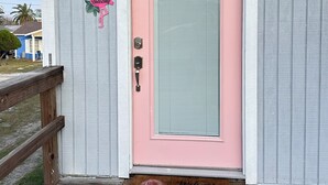 A pink door with a frosted glass panel, a metal bell, and a 'Welcome' sign with a flamingo.