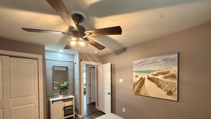 A bedroom with a bed, a ceiling fan, a bathroom with a shower, and a hallway leading to another room.