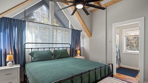 A bedroom with a bed, a nightstand, a lamp, a ceiling fan, and a window with curtains. - Warren VT Chalet for Ski, Summer + Fall Fun, WIFI (Warren)