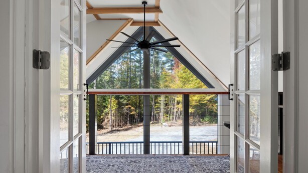 A spacious entryway with a high ceiling, a large fan, and a view of a forested area through a glass door. - Warren VT Chalet for Ski, Summer + Fall Fun, WIFI (Warren)