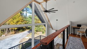 A room with a large window, a wooden ceiling beam, a ceiling fan, a desk, a chair, and a rug. - Warren VT Chalet for Ski, Summer + Fall Fun, WIFI (Warren)