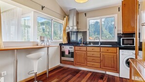 A modern kitchen with wooden cabinets, a stainless steel oven, a microwave, and a washing machine. - Landure Penthouse by Homie (São Vicente)