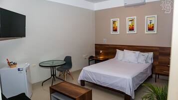 Una camera d'albergo con un letto, una scrivania, una sedia, un tavolino, un frigorifero e opere d'arte appese al muro.