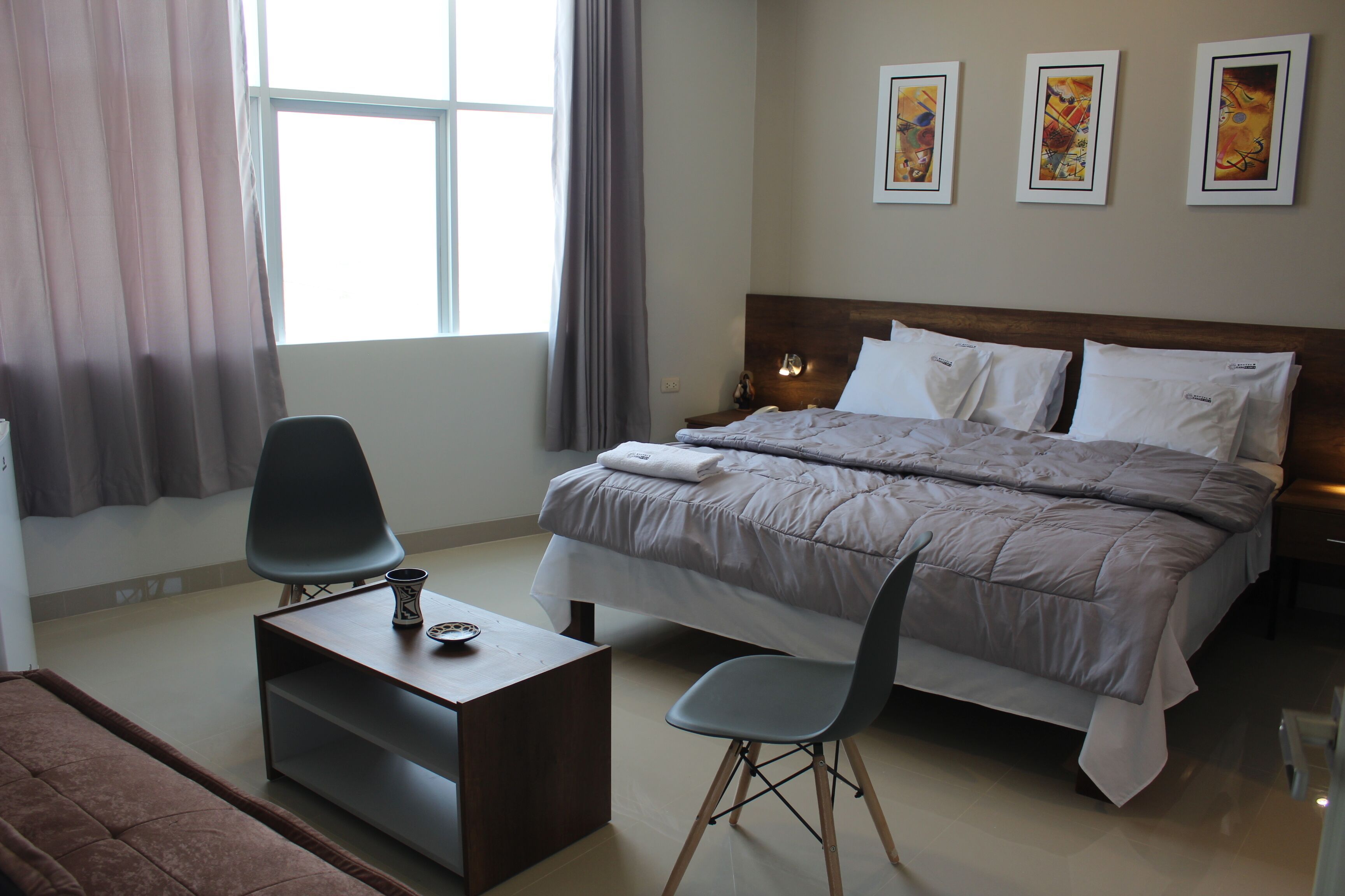 A hotel room with a bed, a desk, a chair, and a window with curtains.
