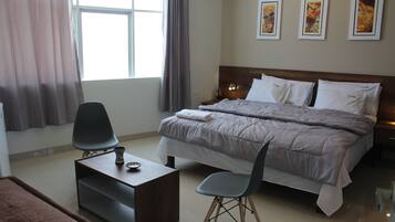 A hotel room with a bed, a desk, a chair, and a window with curtains.