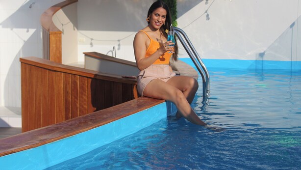 A person sitting by a poolside with a wooden deck and a metal railing. - Sechura Hotel Casa Blanca Piscina Garaje (Sechura)
