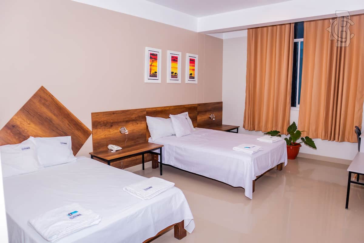 A hotel room with two beds, a wooden headboard, a potted plant, and artwork on the wall.