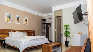 A hotel room with a bed, a wooden bench, a TV, a plant, and a wardrobe. - Sechura Hotel Casa Blanca Piscina Garaje (Sechura)