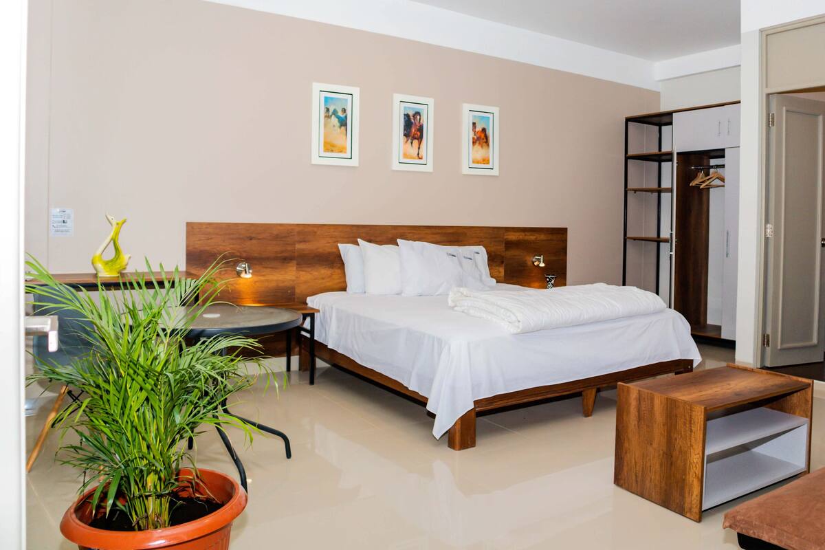 A hotel room with a wooden bed, a bedside table, a potted plant, and a wardrobe.