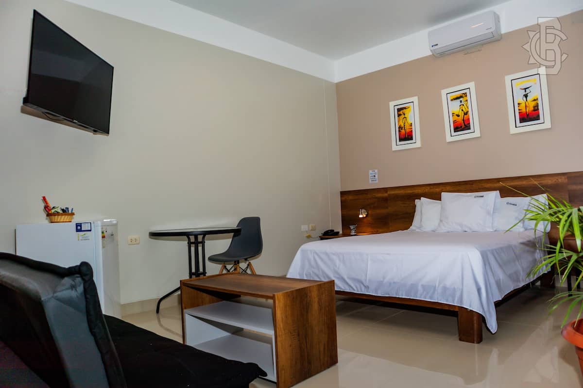 A hotel room with a bed, a desk, a chair, a TV, and artwork on the wall.