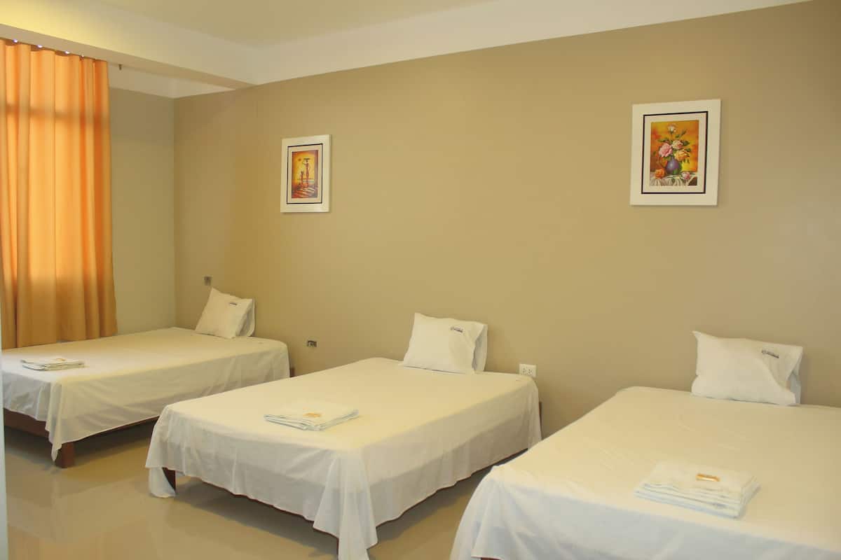 A hotel room with three single beds, each with a white bedspread and pillow, and two framed artworks on the walls.