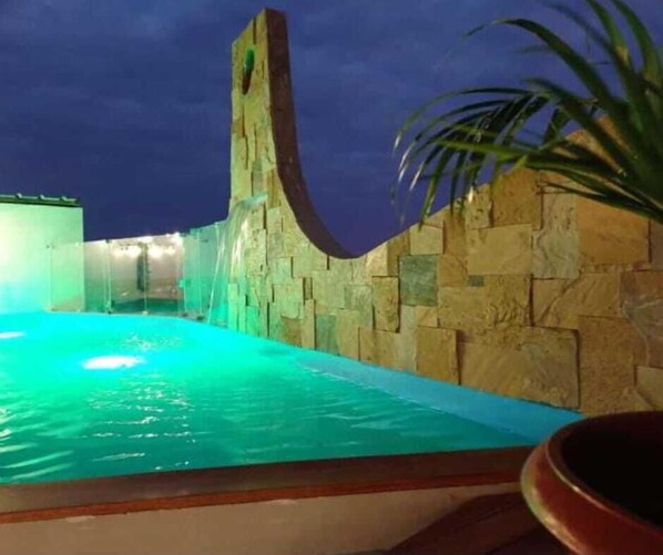 Une piscine avec un mur en pierre et une cascade décorative.