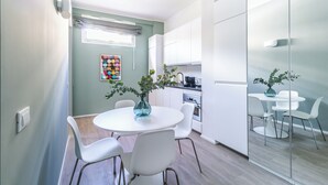A modern kitchen with white cabinets, a dining area with a round table and chairs, and a small window with curtains. - Pirandello 4 - Studio Apartment, Sleeps 4 (Milano)