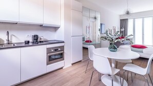 A modern kitchen with white cabinets, stainless steel appliances, and a dining area with white chairs and a table. - Pirandello 4 - Studio Apartment, Sleeps 4 (Milano)