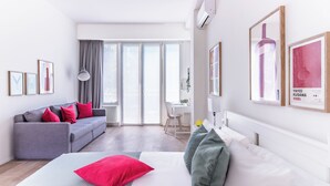 A modern hotel room with a bed, grey sofa, and a dining area. - Pirandello 4 - Studio Apartment, Sleeps 4 (Milano)