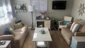 Ein Wohnzimmer mit einem beigefarbenen Sofa, einem weißen Couchtisch und einem an der Wand montierten Fernseher.