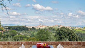 An outdoor dining area with a table and chairs, overlooking a historic town with a prominent tower and buildings.