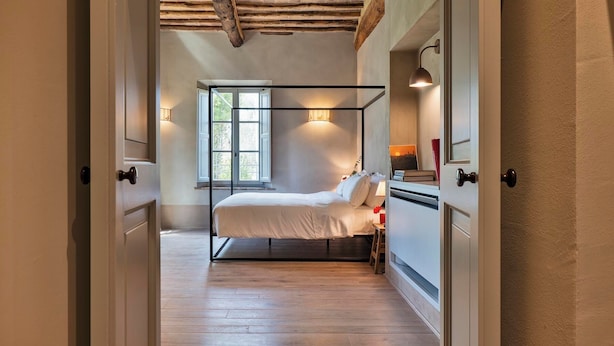 A bedroom with a four-poster bed, a window with natural light, and a wooden ceiling.