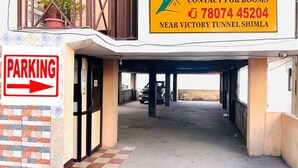 Un bâtiment avec une enseigne indiquant « Hanu Vatika », un panneau indiquant où se renseigner pour la location de chambres et un panneau de signalisation pour le stationnement.