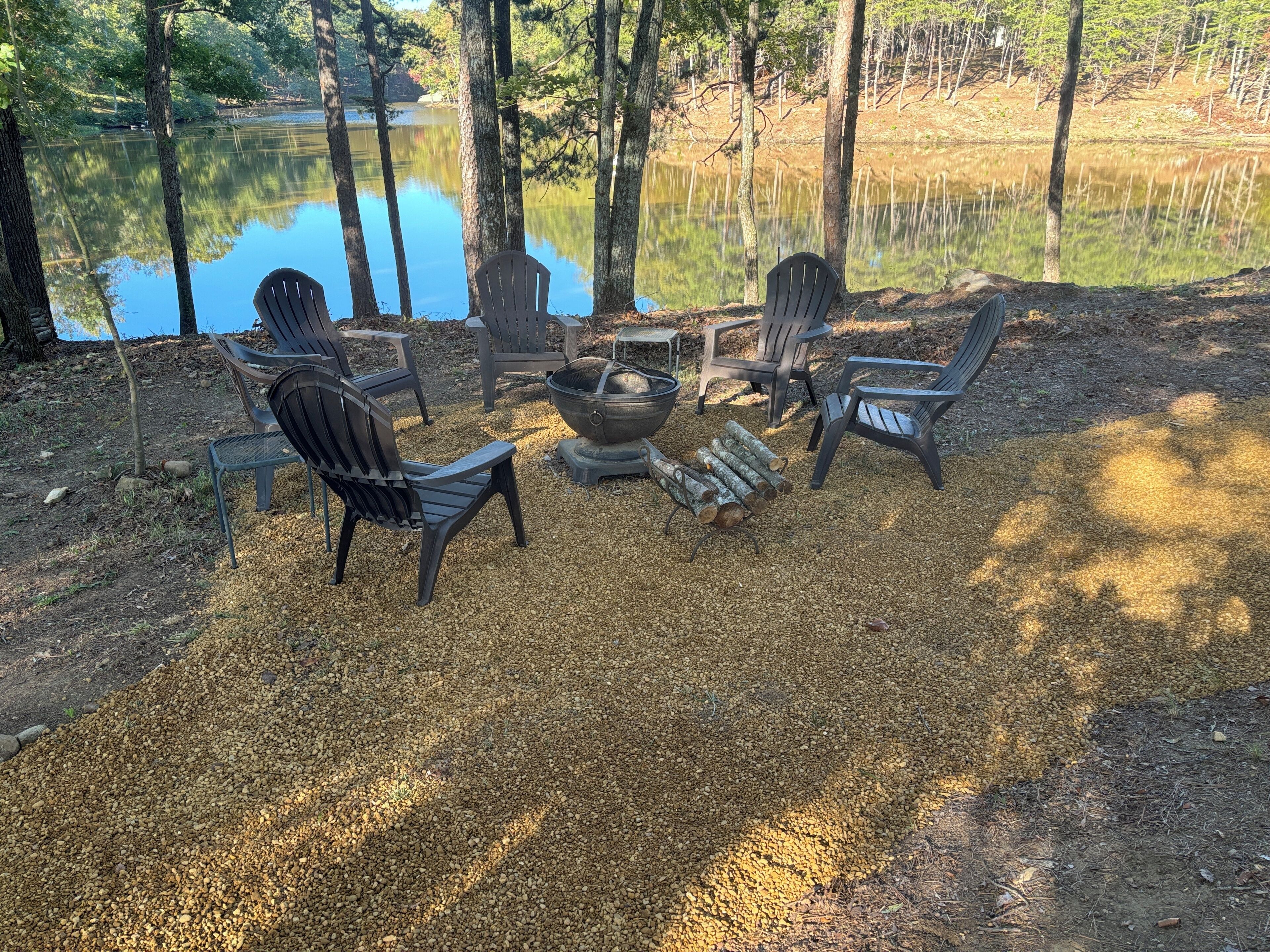 Sitzplatz am Seeufer mit Adirondack-Stühlen und einer Feuerstelle, umgeben von Kies.