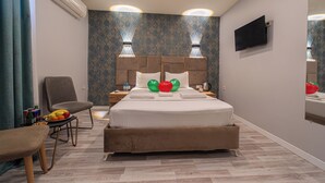 A hotel room with a bed, a chair, a table with fruit, an air conditioner, a wall-mounted TV, and patterned wallpaper. - Casa Nova Hotel (Istanbul)