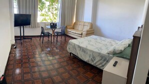 A room with a bed, a sofa, a TV, and a small table with chairs. - Best location facing the sea in Barra  (Barra da Tijuca Rio de Janeiro)