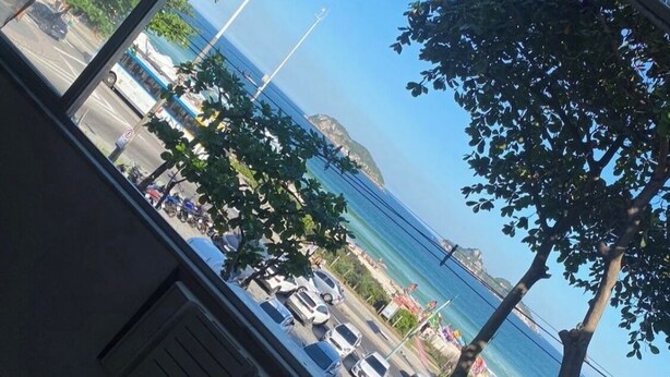 A view from inside a building looking out to a beach with parked cars and trees. - Best location facing the sea in Barra  (Barra da Tijuca Rio de Janeiro)